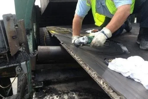 Conveyor Belt Engineer Repairing a Damaged Conveyor Belt Using a Grinder to Cut the Damaged Section of Conveyor Belt